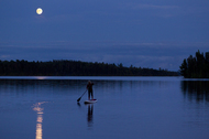 A woman goes for a stand up paddleboard trip at night under a full moon on a small lake in Ontario, Canada.