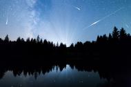 Shooting stars on a dark night sky reflected in a lake.