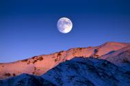 Moon rising over snowy mountains.