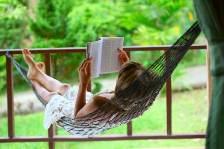 Young woman reading a book lying in hammock.
