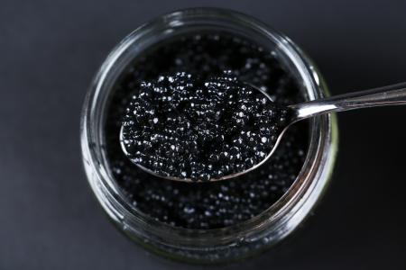 Jar of black caviar and spoon with black caviar on dark background.