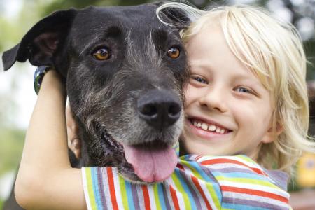 Happy young boy lovingly hugging his pet dog.