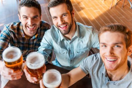 Three happy young men in casual wear toasting with beer.
