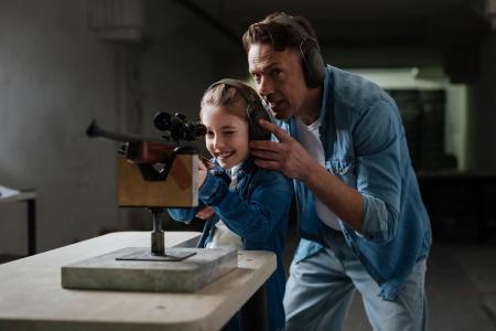 Father advices his daughter on how to aim a rifle at a shooting range.