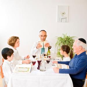 En familie på fem sitter rundt et dekket bord, også kalt seder, med hebraiske tekstbøker.