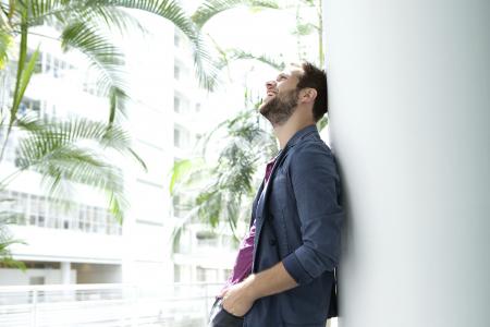 Happy young man leaning against wall in bright building.