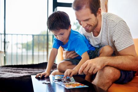 Smiling dad and son building puzzle together.
