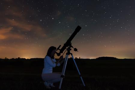 A woman looking at the stars in the night sky through a telescope.