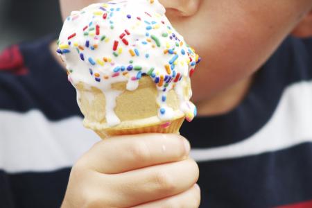 A young child's hand holding a dripping ice cream cone with colorful sprinkles.