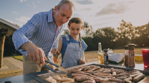 A father and a young girl cooking sausages on a grill in an Australian park.
