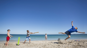 Family playing cricket on the beach in the sand with the sea behind them.