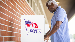 Older black man voting in a voting booth. Image of the American flag and the words 