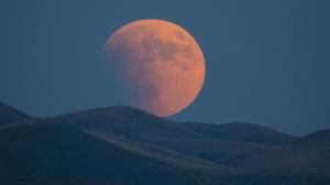A partially red Moon rising from behind mountains.