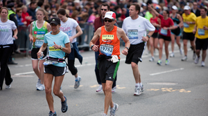 Older man and younger woman in running gear and bibs participating in the Boston Marathon near the one-mile remaining mark in Kenmore Square.