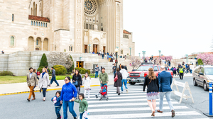 People, families, mothers, and children walking by basilica of the National Shrine of the Immaculate Conception Catholic church street road on Easter Sunday.