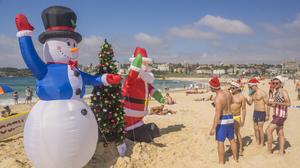Inflatable snowman, Christmas tree, and Santa with beachgoers in the sand at Bondi beach.