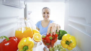 Woman reaching for strawberries in a fridge.