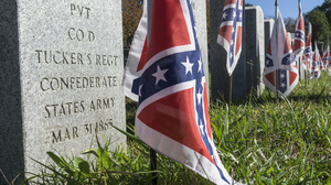 Close up of a grave stone for a confederate soldier with a confederate flag put in the ground before it.