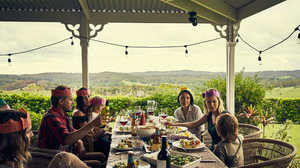 A family in party paper hats around a table on a porch in Australia.