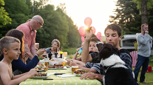 Celebration time for this three generation real family outdoors in summer. Big dinner is ready, people coming to the table. Young man feeding the dog. Horizontal waist up shot. This was taken in Quebec, Canada.