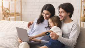 Family of three shopping online. Kid is sitting between the parents with the laptop on the mother's lap and dad is holding the credit card. Kid is pointing to the screen.