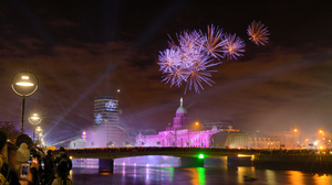 Fireworks in the night sky over Custom House in Dublin. People watching from bridge over illuminated river.