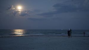 People use a smartphone to photograph the moon and sea at Jetty Park in Cape Canaveral, Florida.