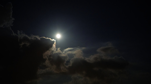Bright moon in a dark cloudy sky with te clouds reflecting the moonlight.
