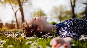 A young girl laying in the grass in the spring sun surrounded by daisies.