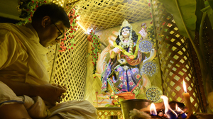 A man sitting by a statue of the goddess Saraswati lit up in yellow.