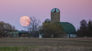 Moonrise over a farm with a barn in the backdrop.