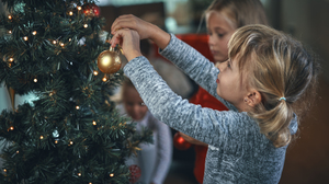 Two little girls decorating the Christmas tree with ornaments and Christmas lights.