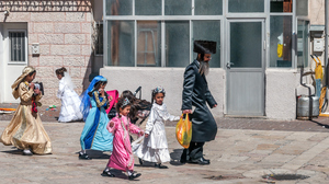 Jewish man in traditional clothing walking down a street, followed by girls in dresses