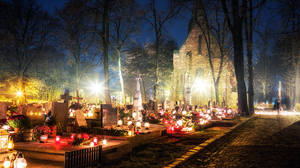 A churchyard at night lit up by burning candles on the graves.
