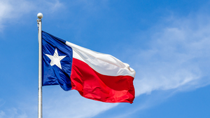 Texas State flag on the pole waving in the wing against blue sky and white clouds.