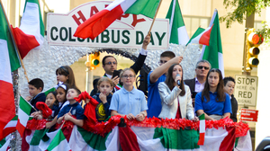 People standing on a parade float, decorated with red, white and green flags.
