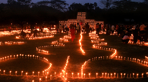 A large area with lighted candles set up in a formation on the ground outside after sunset.