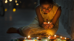 A little indian girl sitting on the floor and lighting up dipa oil lamps for the Diwali celebration.