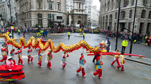 Several people walking in the street, carrying a colorful dragon to perform the 