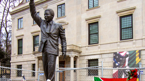 A statue of Nelson Mandela standing in front of a big stone building.