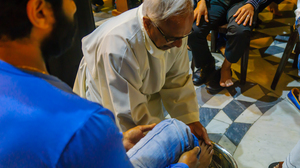 Priest sitting on the floor washing the feet of a congregation member in a Holy Thursday ceremony in church.