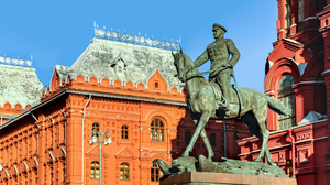Bronze sculpture of General Zhukov on a horse with red stone buildings and a blue sky in the background.