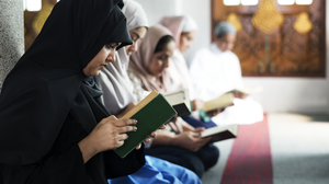 Four muslim women and a man is sitting on the floor in a mosque, reading in the Koran.