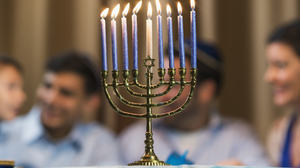 Menorah with all 9 candles lit in front of an out of focus family celebrating Hannukah.