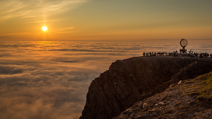 Photo of people on a cliff looking at the midnight Sun in Nordkapp, Norway.