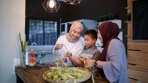 A Muslim sister, brother and mother making food together at a kitchen counter.
