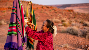 Elderly Navajo woman weaving a traditional native American blanket in the desert.
