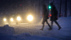 Two people walking in bad winther weater, cars approaching them.