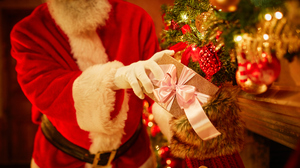 Santa Claus placing a wrapped gift into a Christmas stocking by a decorated tree