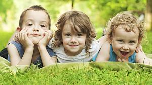 Three young children lying in the grass smiling.